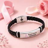 Breast Cancer Awareness braided leather bracelet with a pink ribbon engraved stainless steel plate displayed on a soft pink background with flowers and a pink awareness ribbon