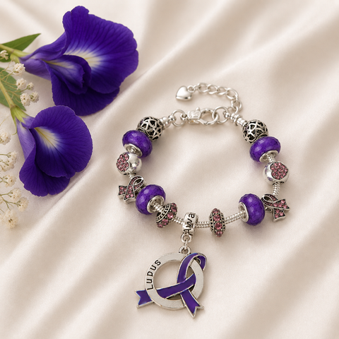 Lupus Awareness Luxury Charm Bracelet with purple beads, silver charms, purple awareness ribbon pendant, and butterfly pea flowers on ivory satin